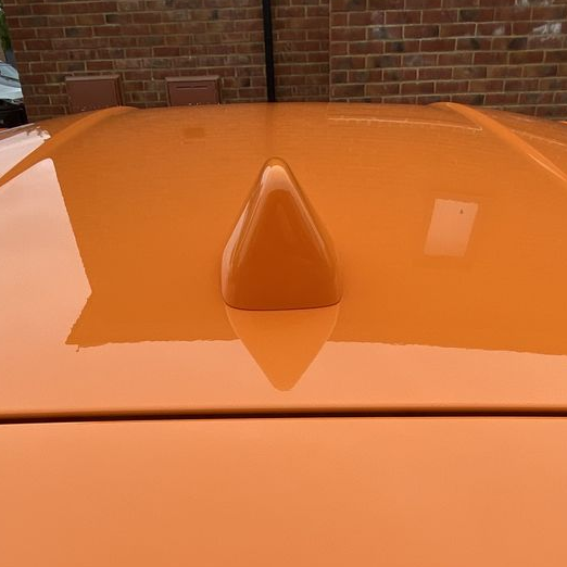 Orange car with a Shark Fin aerial on top against a brick wall.